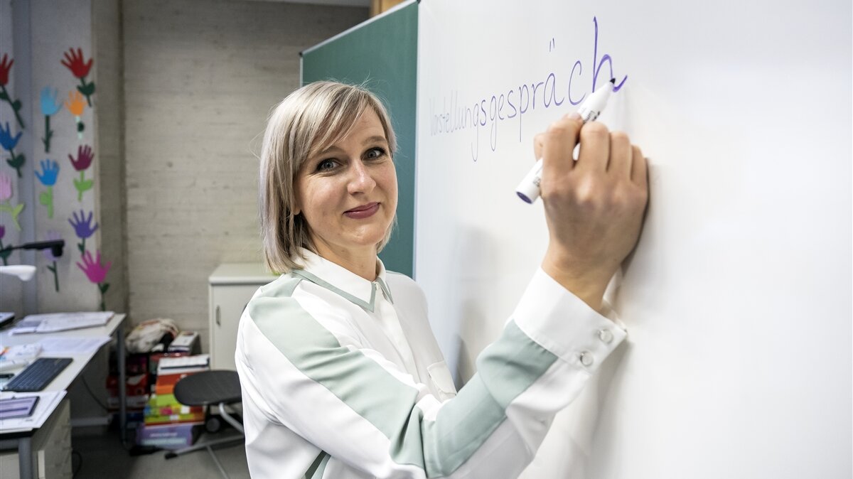 Eine Lehrerin schreibt das Wort „Bewerbungsgespräch“ an ein Whiteboard.