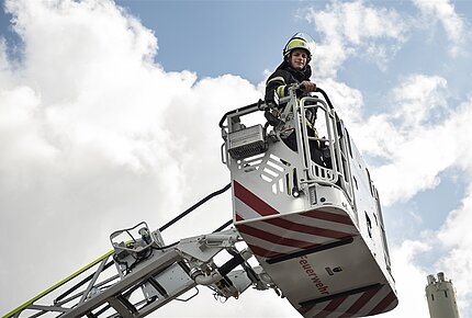 Ein Feuerwehrmann steht in einem Rettungskorb, der nach oben gefahren wird.
