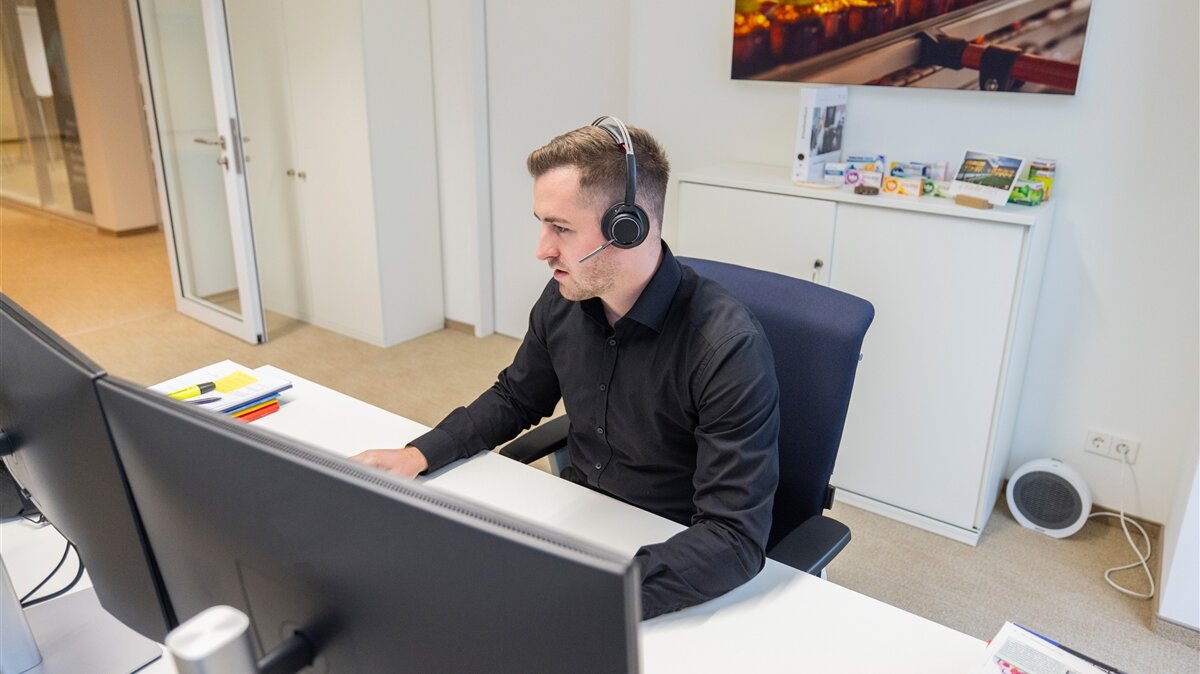 Ein junger Mann arbeitet mit Headset am Computer im Büro.