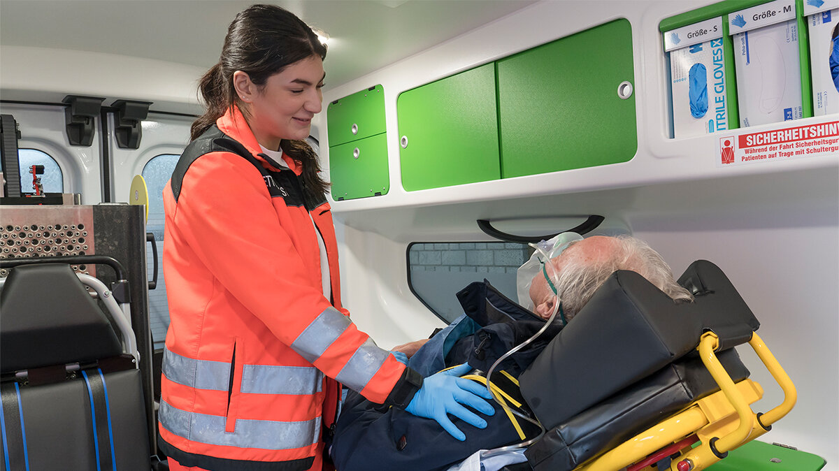 Eine junge Frau behandelt einen älteren Mann auf einer Liege im Krankenwagen.