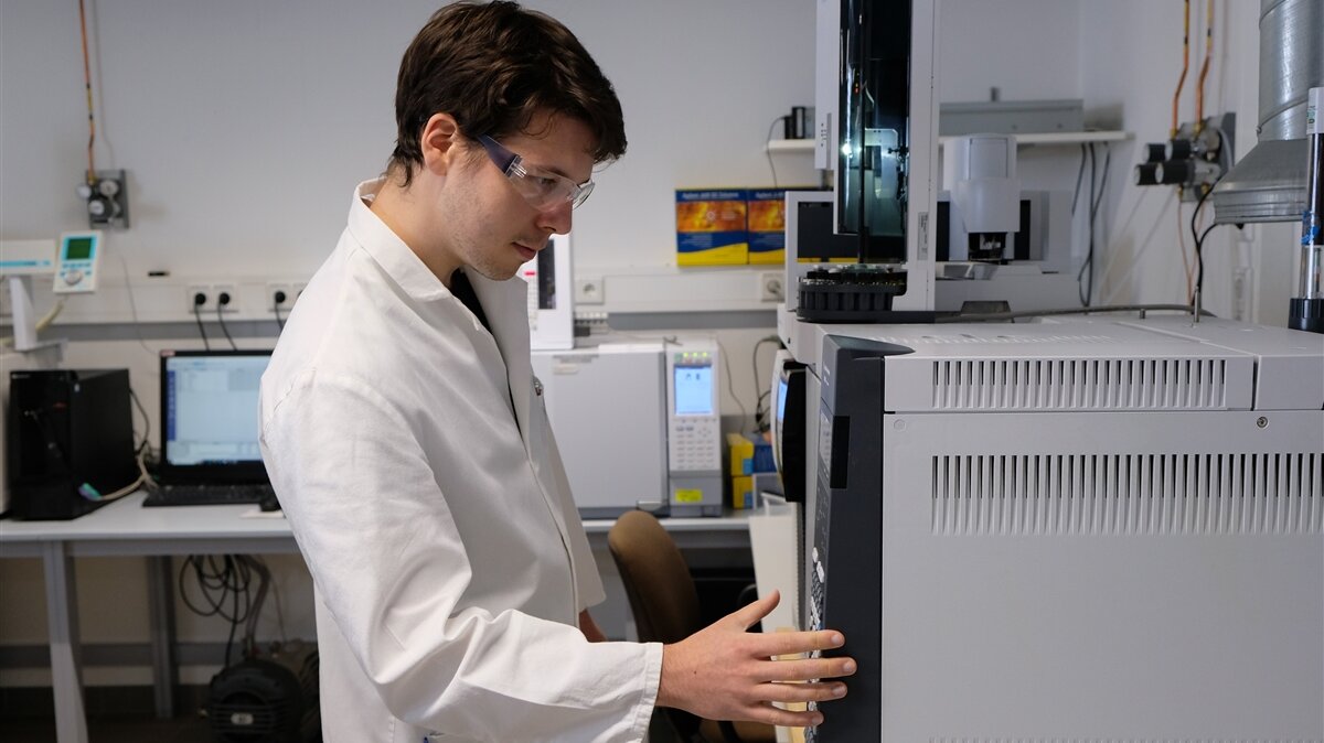 Ein Mann in Laborkittel legt die Hand an ein chemisches Gerät.
