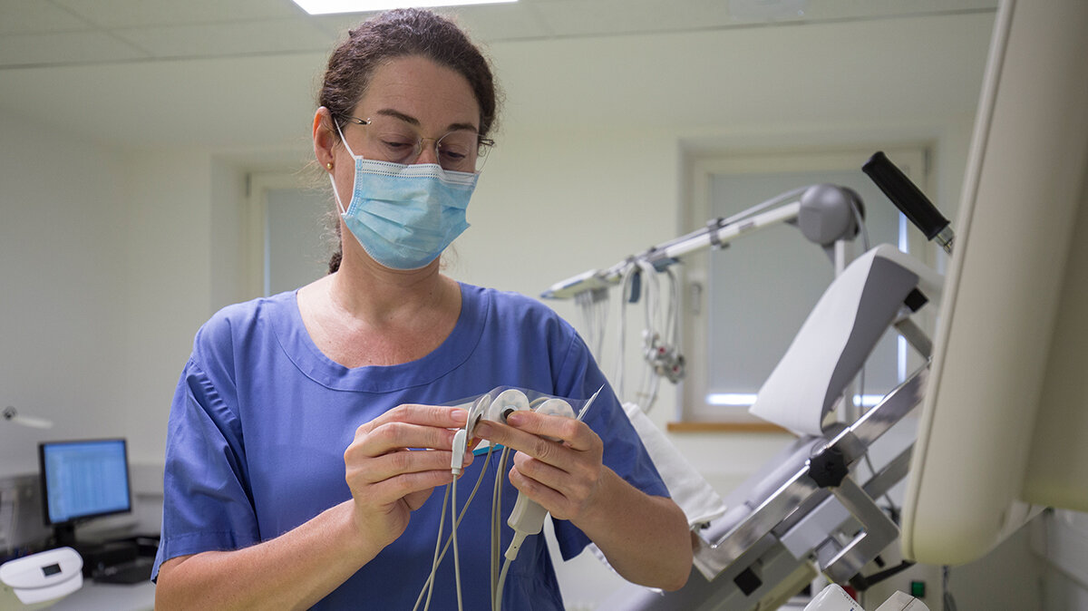 Eine Frau mit OP-Maske hält mehrere Elektroden in den Händern und bereitet sie vor.