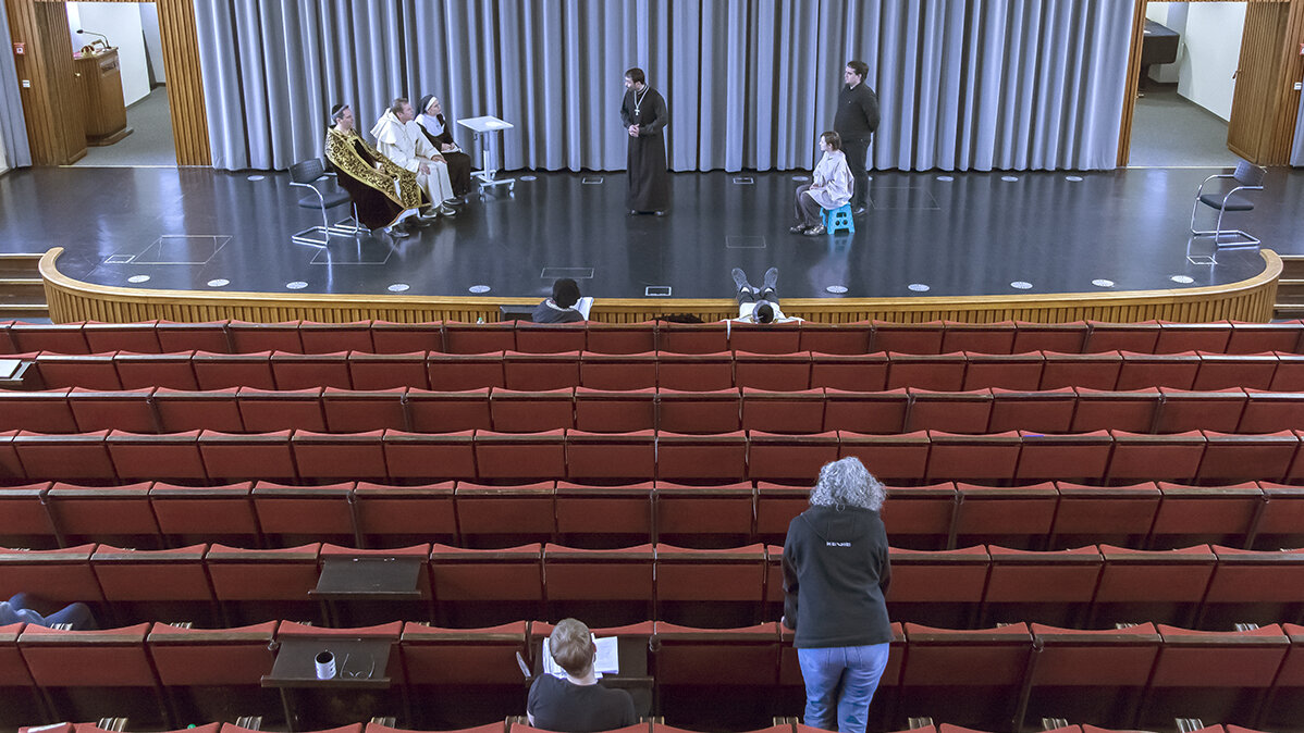 Eine Gruppe Menschen führt vor Publikum ein Stück auf einer Bühne auf. 