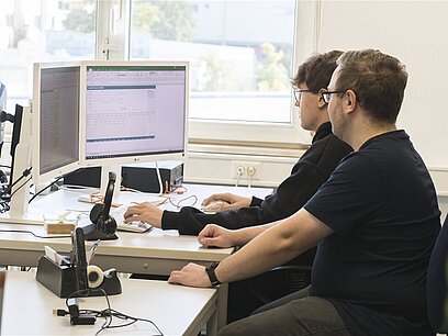 Zwei junge Männer schauen sich etwas auf einem Computer an.