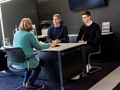 3 Personen sitzen an einem Tisch und besprechen sich.