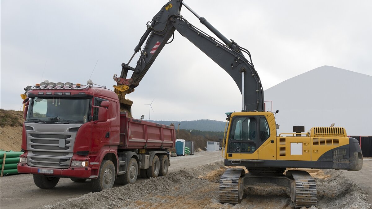 Auf einer Baustelle lädt ein Bagger Schotter in einen Lastwagen.