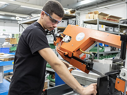 Ein junger Mann mit Schutzbrille arbeitet an einer Sägemaschine. 