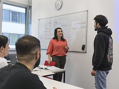 Ein junger Mann und eine Frau stehen in einem Klassenraum vor einer Tafel  und schauen sich an.