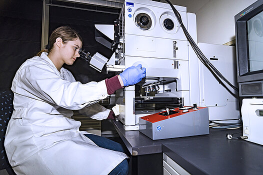 Eine junge Frau betrachtet im Labor etwas durch ein Mikroskop. 