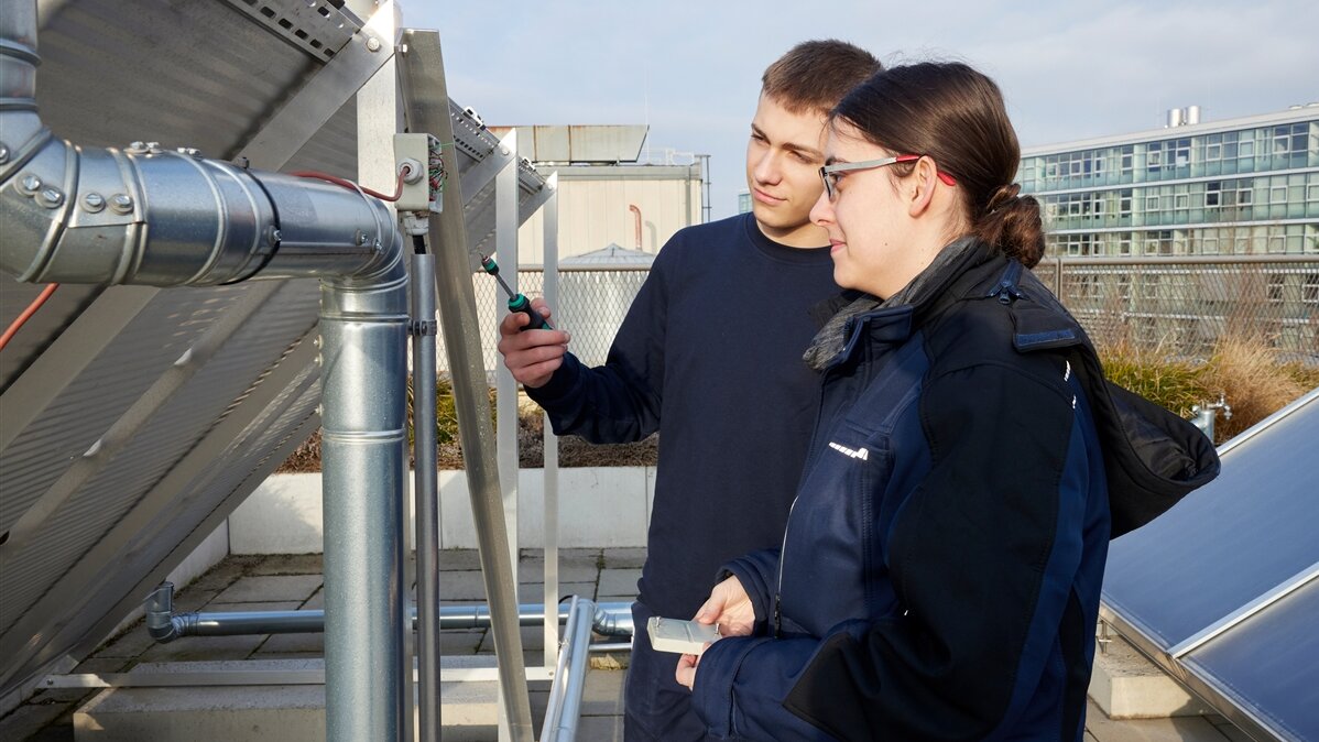 Eine junge Frau und ein junger Mann nehmen Messungen an einer Photovoltaik-Anlage vor.