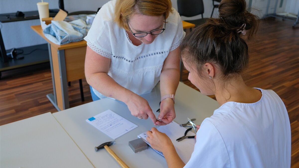 Die Ausbilderin zeigt Marie-Louise, wie sie den Draht für eine Nagelspange biegen muss.