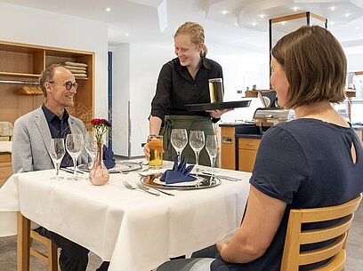 Eine junge Frau bringt Gästen Getränke an den Tisch.