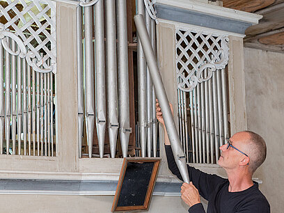 Ein Mann baut eine Pfeife in eine Orgel ein.