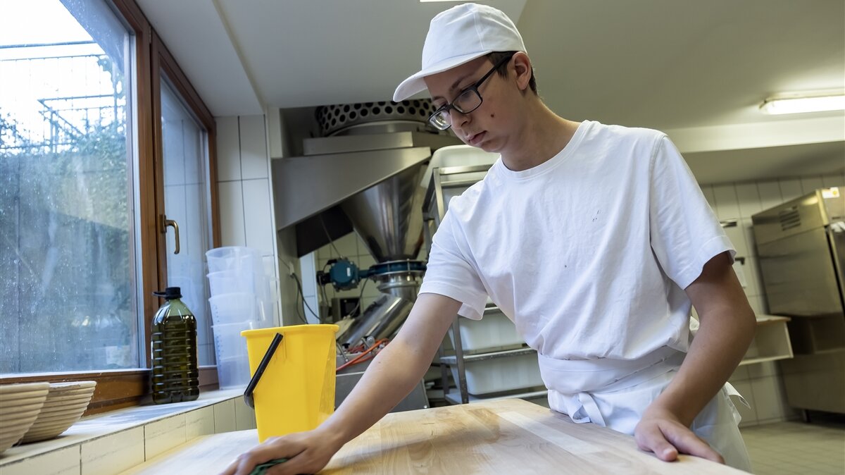 Ein junger Mann wischt einen Tisch mit einem Lappen ab.
