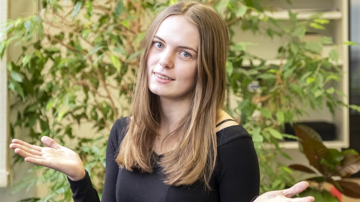Eine junge Frau schaut in die Kamera und macht eine ratlose Geste.