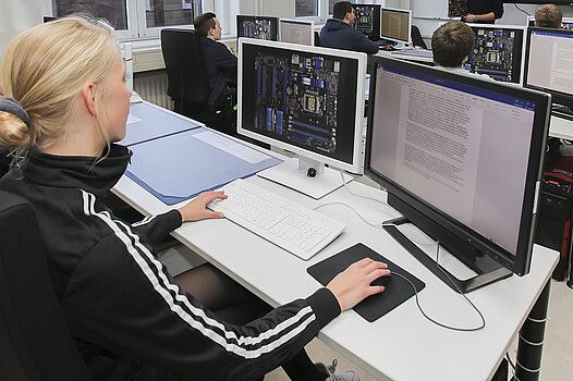 Eine junge Frau sitzt vor zwei Bildschirmen und programmiert am Computer.