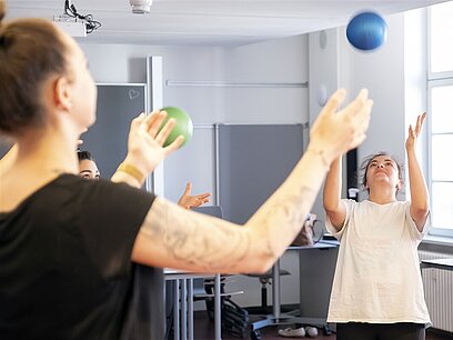 Zwei Frauen werfen sich einen Gymnastikball zu während einer Übung.