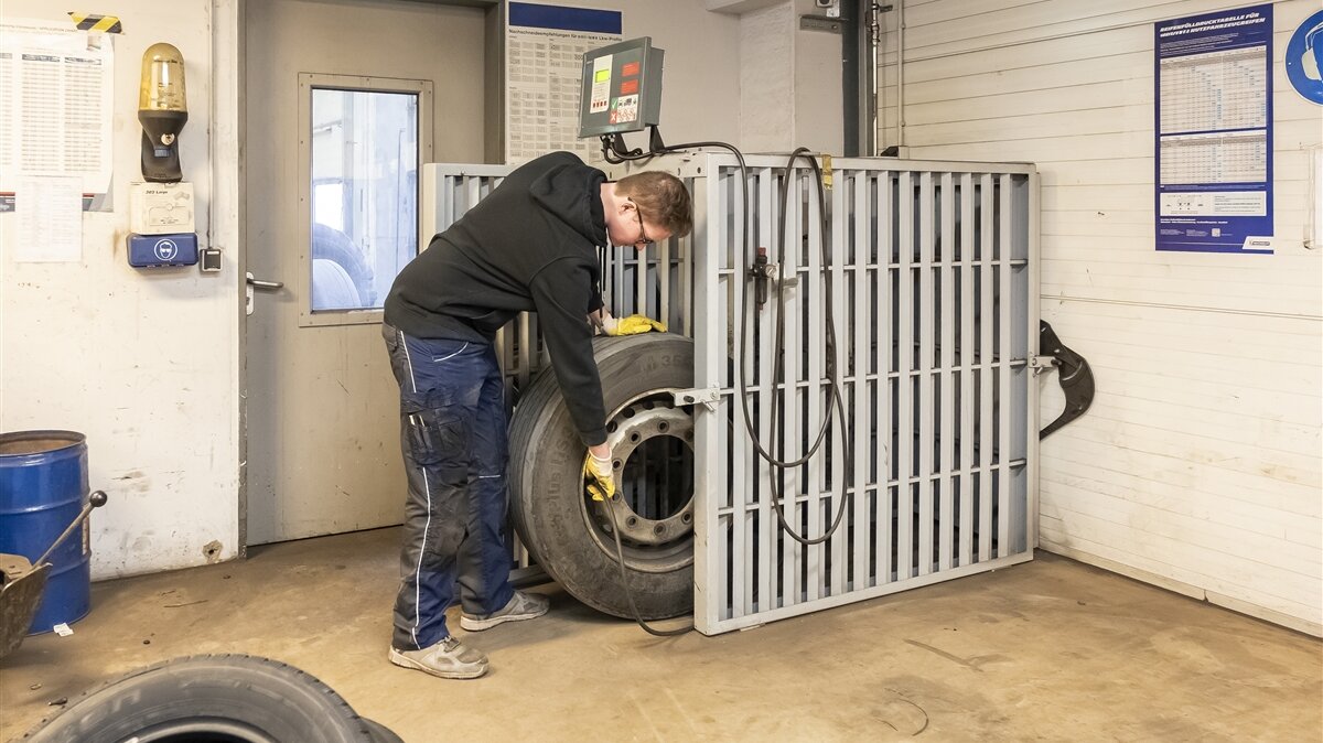 Tobias trägt Schutzhandschuhe und befüllt einen LKW-Reifen im Füllkäfig.
