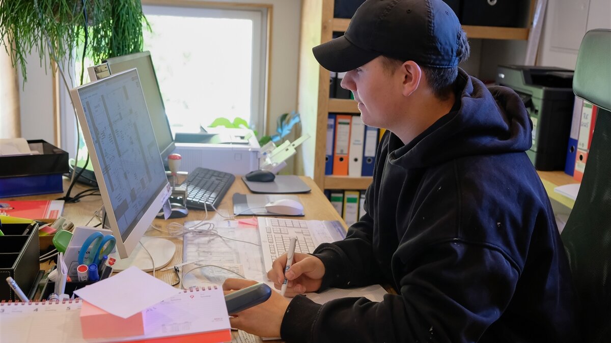 Julian arbeitet am Computer in einem Büro und sitzt am Schreibtisch.