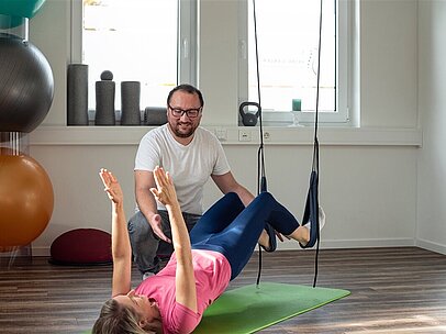 Ein Fitnesstrainer unterstützt eine Frau bei einer Übung. 