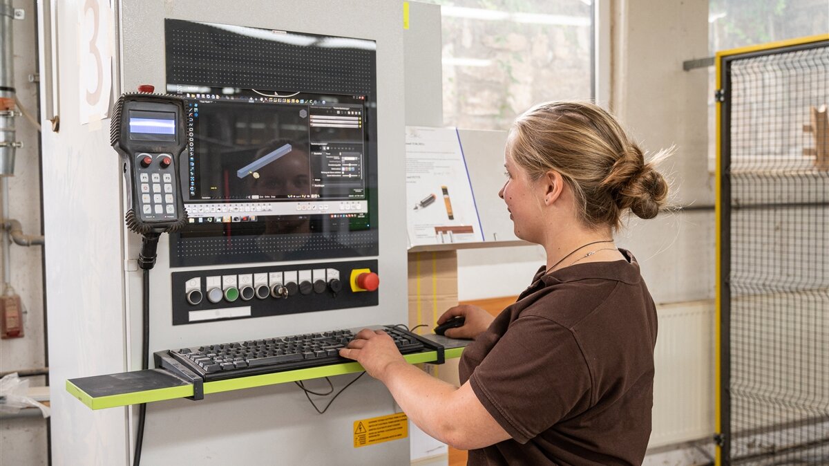 Sarah programmiert mit einer computergesteuerten CNC-Maschine die Position der Bohrlöcher für ein Holzstück.