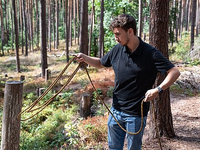 Ein junger Mann befestigt ein Seil an einem Baum im Wald.