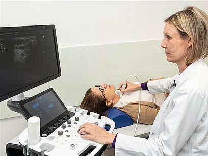 Eine Frau untersucht die Schilddrüse einer anderen Frau mit Ultraschall.