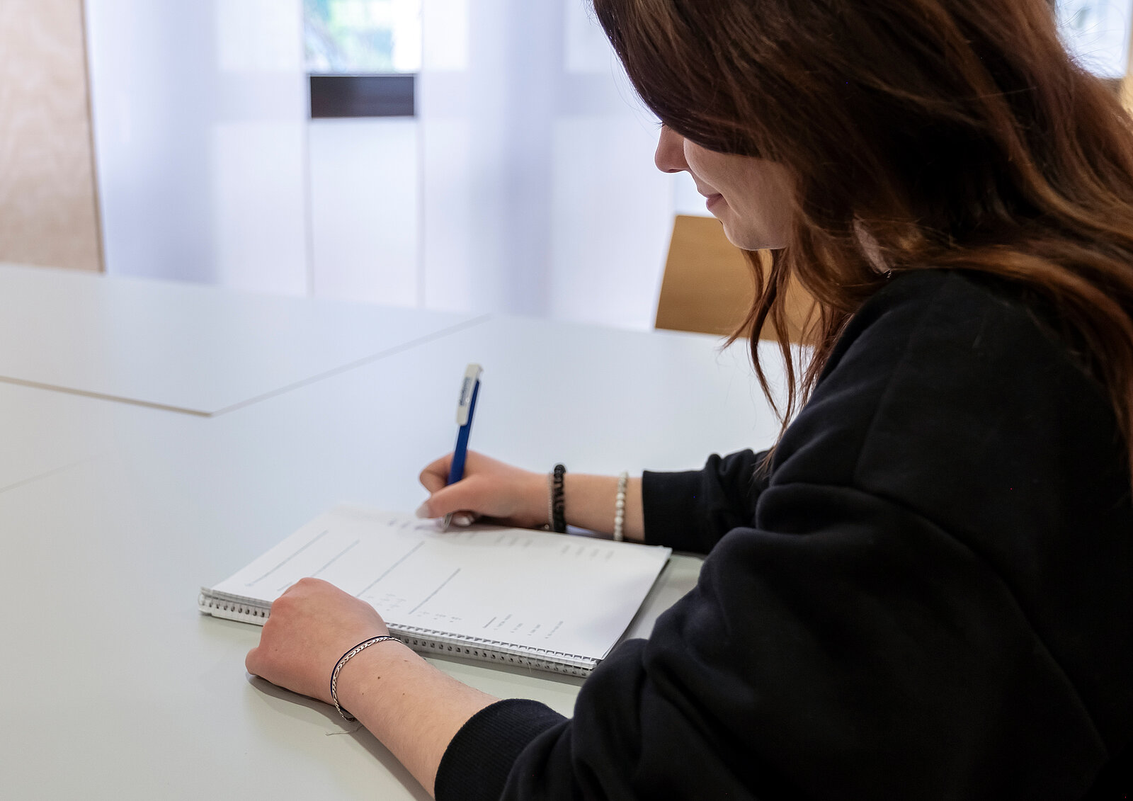 Eine junge Frau sitzt am Tisch und füllt ein Formular aus.