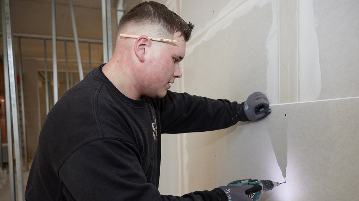 Benjamin schraubt mit einem Schnellbauschrauber Gipsplatten an die Wand.