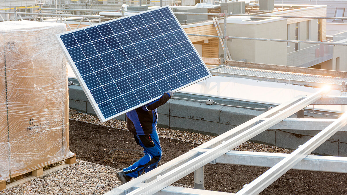 Eine Person trägt ein Solarpanel auf einer Baustelle.