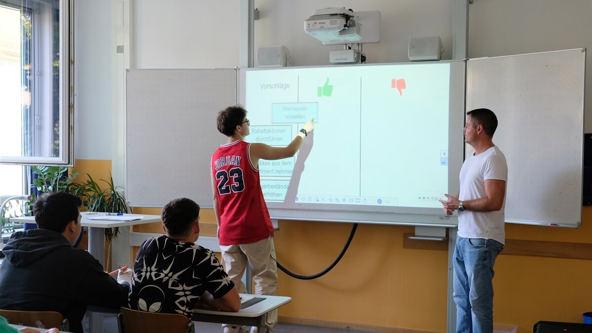 Ein Schüler zeigt dem Lehrer und der Klasse etwas an der Tafel. 