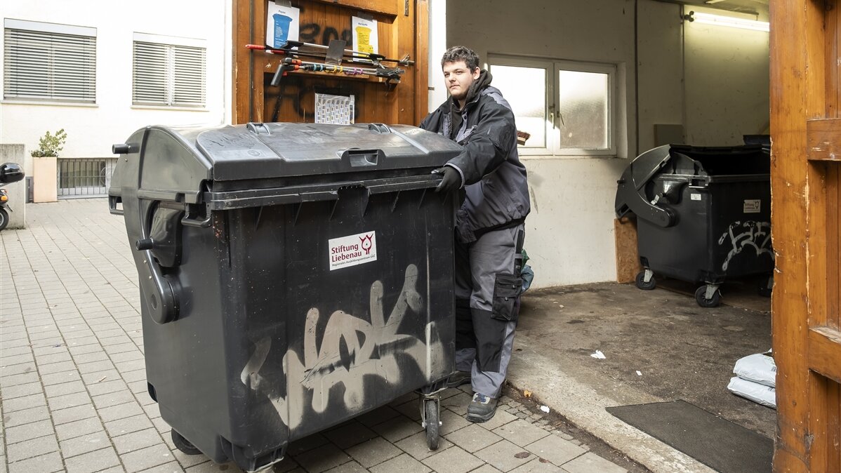 Frank bringt eine Mülltonne mit Restmüll aus der Garage an die Straße.