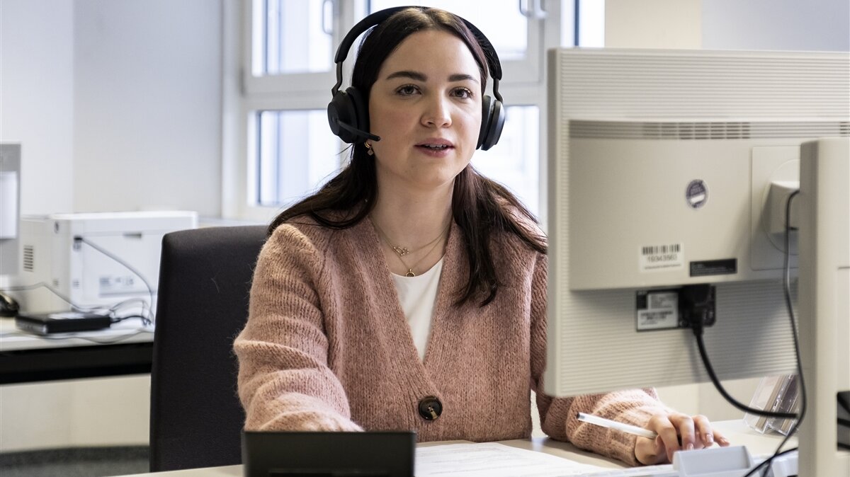 Eine junge Frau führt am Computer im Büro ein Gespräch mit Headset.
