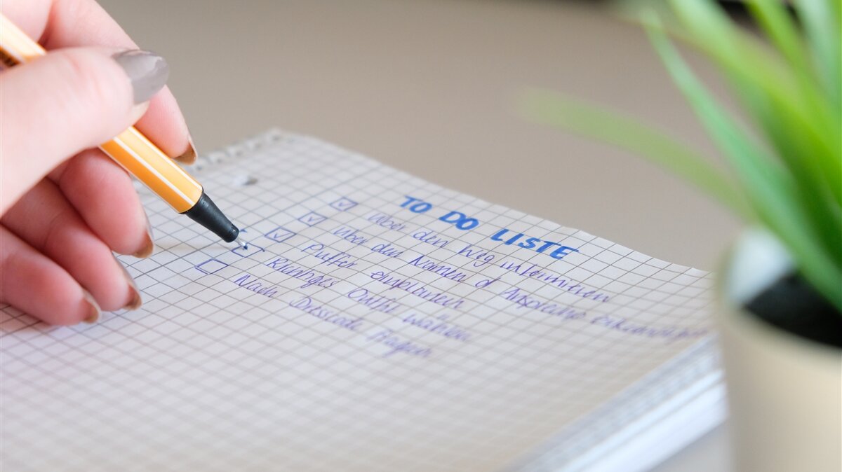 Eine Person schreibt eine Liste mit einem Stift auf einem Block.