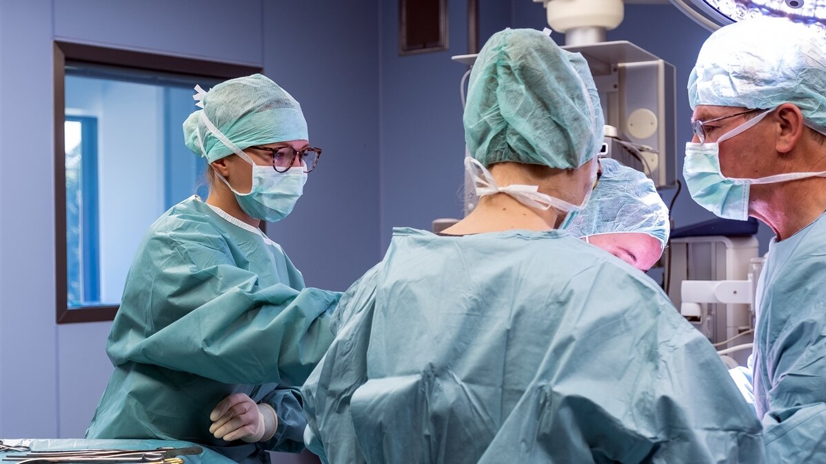 Eine junge Frau reicht einem Chirurgen während der Operation ein Instrument.