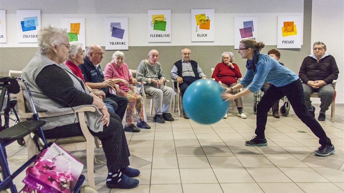 Eine junge Frau aktiviert Senioren in einem Pflegeheim mit einem Ballspiel. 