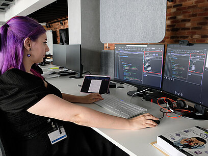 Eine junge Frau programmiert an zwei Computer-Bildschirmen.