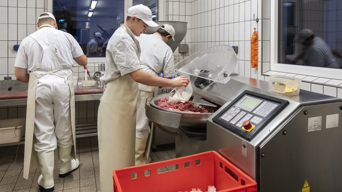 Stefan fügt Gewürze zu der Fleischmasse im Kutter hinzu.