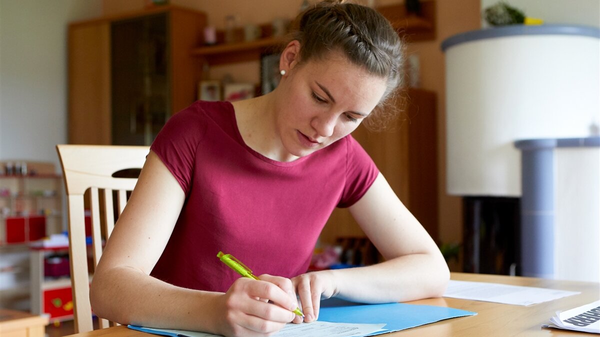 Eine junge Frau sitzt am Tisch und schreibt etwas auf.
