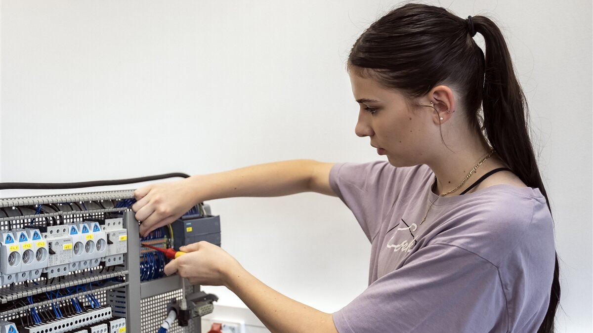 Eine junge Frau arbeitet mit einem Schraubenzieher an einer Schaltstation.