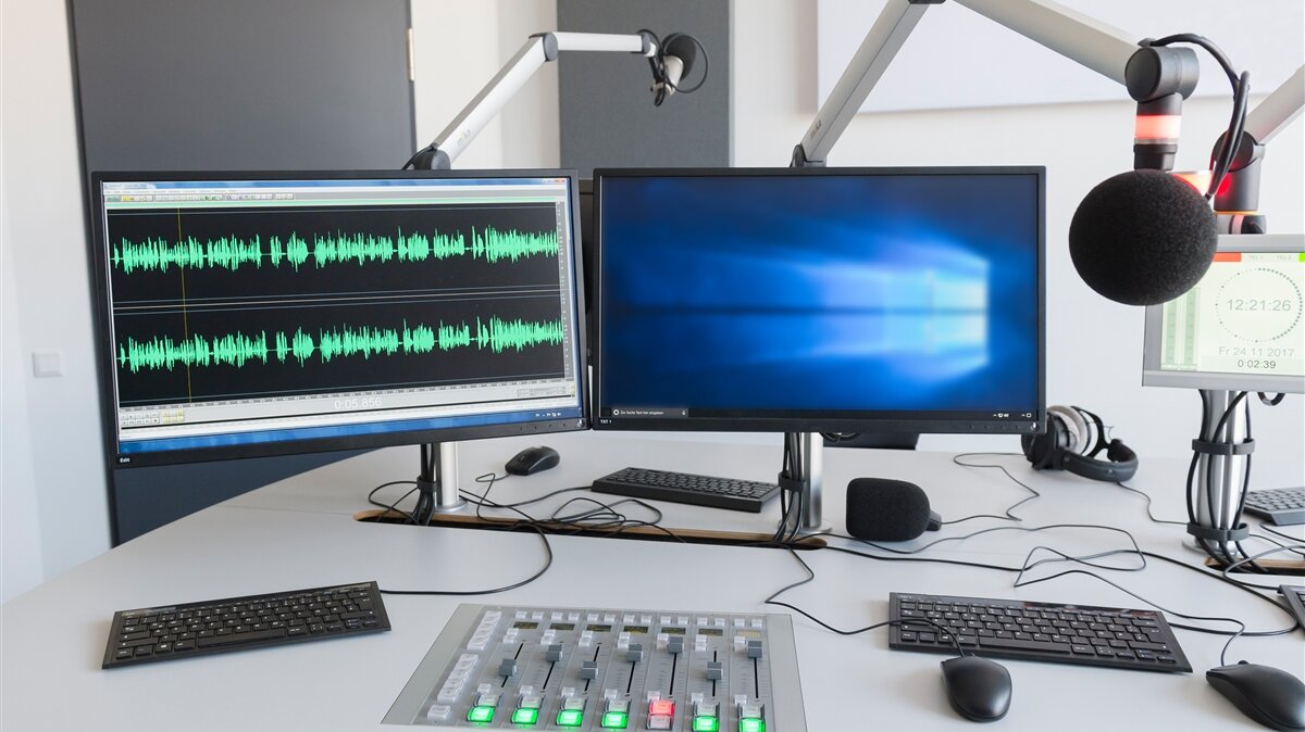 Zwei Computerbildschirme und ein Mikrofon in einem Aufnahmestudio.