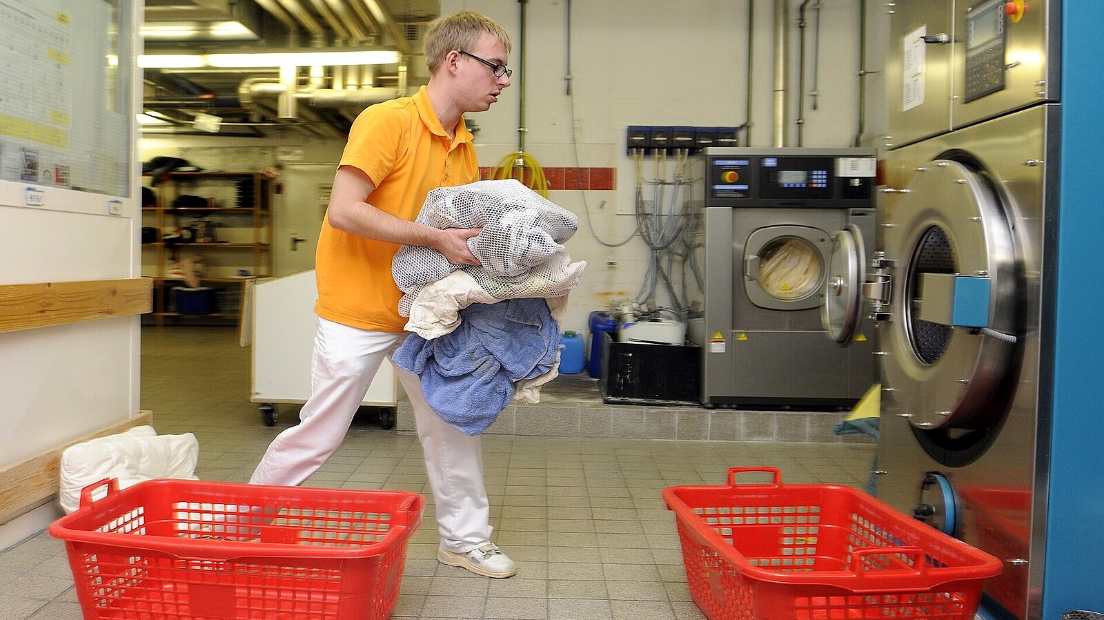 Ein Mann befüllt eine Industrie-Waschmaschine mit einer neuen Ladung an Wäsche.