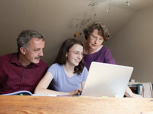 Eine Tochter sieht sich mit ihren Eltern etwas auf dem Laptop an.