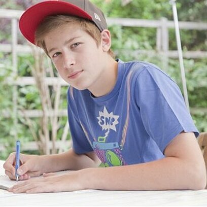 Ein Junge schreibt mit einem Stift auf einen Block.
