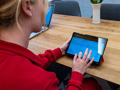 Eine junge Frau arbeitet an einem Tablet und tippt etwas ein.