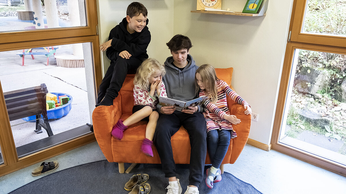 Ein Junge liest Kindern drei Kindern ein Bilderbuch vor.