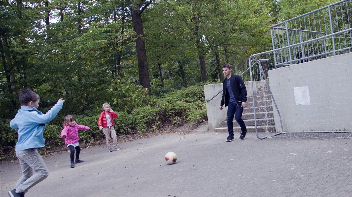Ein junger Mann spielt mit drei Kindern Fußball.