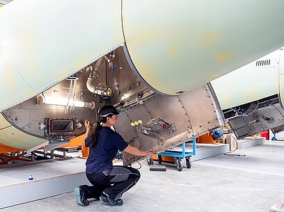 Eine junge Frau arbeitet an einem Bauteil für ein Flugzeug.