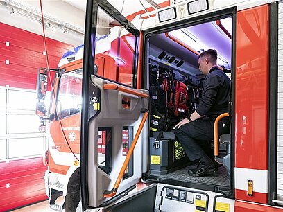 Ein Mann sitzt bei offener Autotür in einem Feuerwehrauto auf einem der Mannschaftssitzplätze.