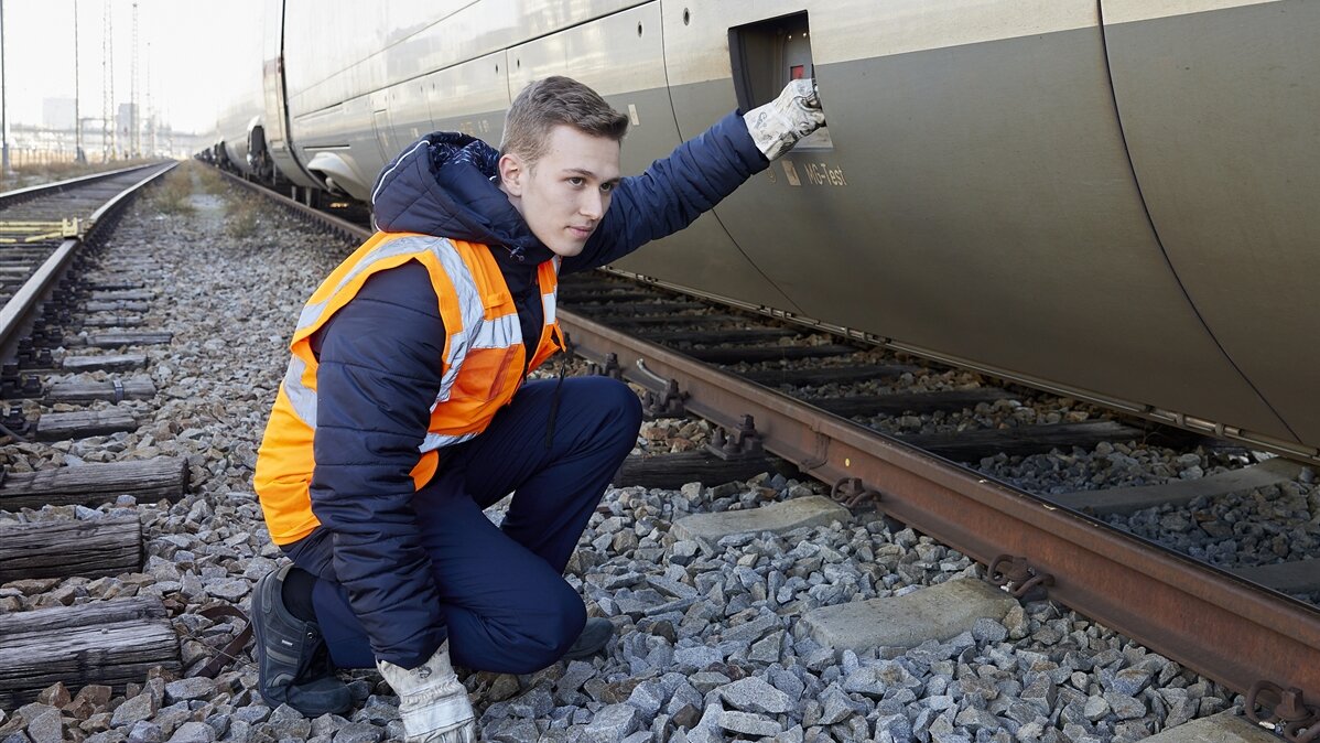 Ein Eisenbahner prüft einen Zug von außen am Gleis.